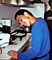A student in the kitchen standing next to the stove.